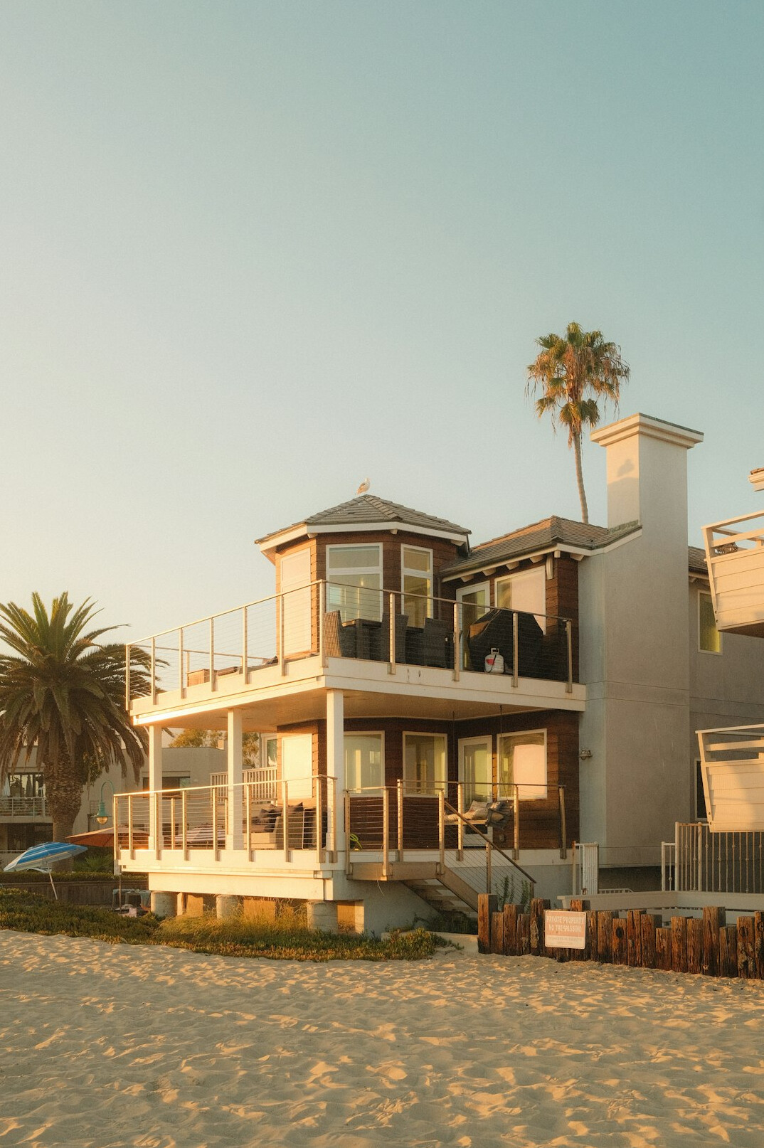Oceanfront estate home with large glass windows at sunset